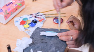 Resim fırçası eğitimi alan ve sanat sınıfındaki ahşap oyuncak bebek üzerinde boya öğrenen öğrencilerin yakın çekim elleri..