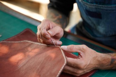 Closeup hand of leather craftsman is carefully to sew a leather bag for a customer., Leather craftsman concept.