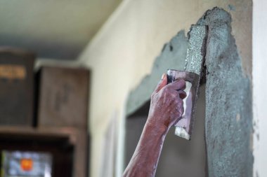 İnşaat alanında havan topu tutan ve duvarları çimentoyla kaplayan inşaatçının elleri.