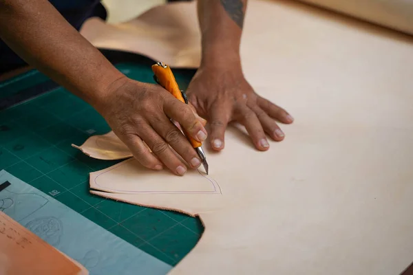 Closeup hand of leather craftsman is carefully using a cutter knife to cut the white leather.