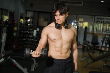 Mükemmel vücutlu Asyalı yakışıklı adam spor salonunda ağırlık çalışması yapıyor..