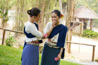Çok güzel bir Taylandlı genç bayan, Tayland 'ın geleneksel kıyafetlerini giyip arka planda sohbet edip alay ediyorlar..