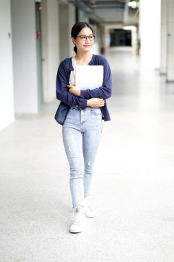Elinde dizüstü bilgisayar olan Asyalı genç bir kız öğrenci okul binası koridorunda yürüyor. Asya okulu kavramı.