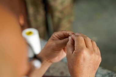 Deri zanaatkârının yakın çekim ve dikiz arkası elleri, bir müşteriye deri ürün dikmek için bir iğneyi dikkatle iplikliyor..