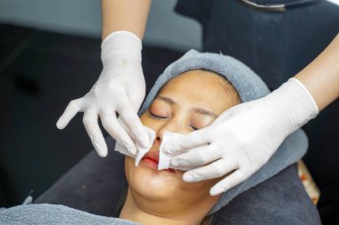 Kozmetik uzmanı, güzellik kliniğindeki kadın müşterinin yüzünü temizlemek için pamuk pedi kullanıyor..