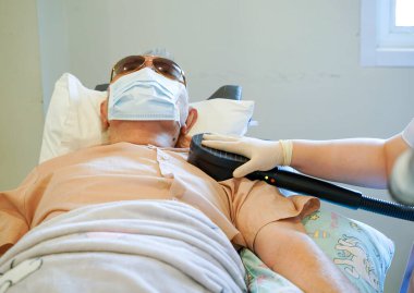 Huzurevlerinde yaşlı bir hastanın omzunda elektriksel kas uyarısı (EMS) kullanan doktorların yakın çekim elleri