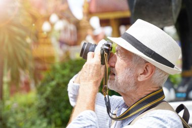 Yaklaş ve hasat et Amerikalı kıdemli turist arka planda güneş ışığıyla Tayland tapınağında fotoğraf çek. Kıdemli turist konsepti