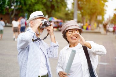 Yakın plan Amerikalı kıdemli turist, şehirde tur rehberiyle güneş ışığı ve bulanık arka plan üzerine bir fotoğraf çekiyor.