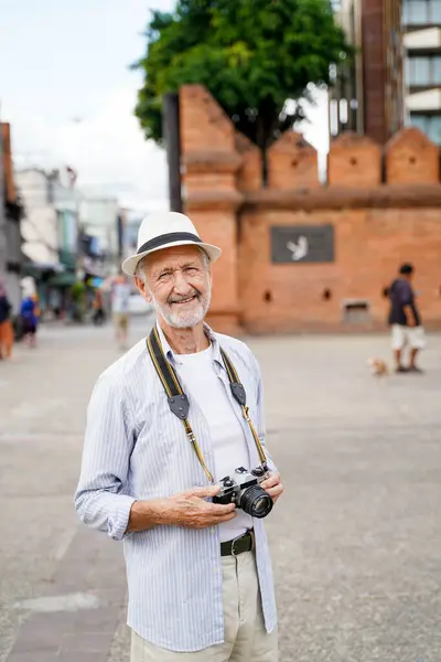 Closeup American senior tourist man acting for photograph on burred the Chiang Mai city gate landmark background. Senior tourist concept