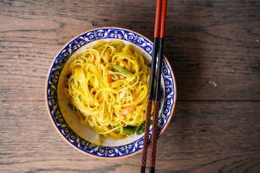 Üst manzara Çin vejetaryen yumurtalı erişteyi Çin vejetaryen festivali için ahşap arka planda seramik kasede karıştırıyor..