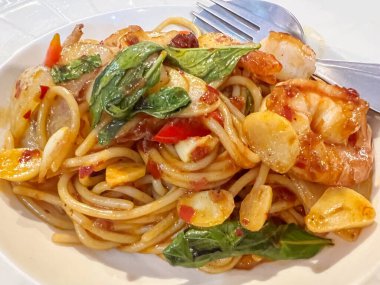 Yakın çekim füzyon karidesler ve mürekkep balıkları beyaz seramik tabakta kızarmış acı biber macunu spagettisi karıştırıyorlar..