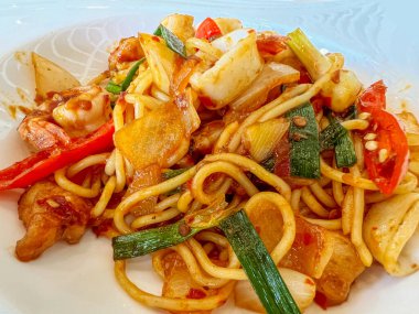 Yakın çekim füzyon karidesler ve mürekkep balıkları beyaz seramik tabakta kızarmış acı biber macunu spagettisi karıştırıyorlar..