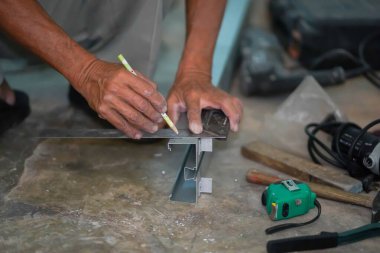 İnşaat alanındaki alüminyum keresteyi kesmeden önce, kalemi kullanarak yapıcının elleri detayları işaretler..