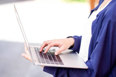 Asyalı genç kız öğrenciyi yakın çekim ve kırpma kıyafetleri içinde açık arka planda dizüstü bilgisayar klavyesi kullanarak ve yazarak.