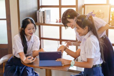Mutluluk grubu neşeli Taylandlı öğrenciler parlak güneş ışığı arka planına sahip tablet üzerinde sosyal bir ağ arıyorlar.