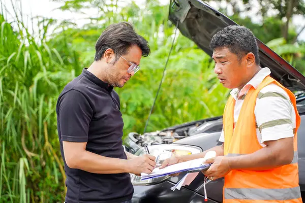 A garage employee inspects a car with a broken engine. and have the owner sign an acknowledgment of the damage and agree to allow the technician to inspect and repair