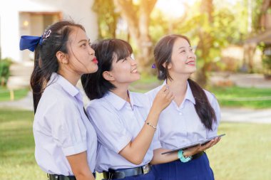 Neşeli ve sevimli Taylandlı öğrencilerden oluşan bir grup açık hava okulunun çimlerine bakıp gülümsüyor, parlak ve bulanık doğa geçmişi olan..