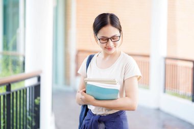 Şirin bir gülümsemesi ve okul binasında ders kitaplarını tutan sıradan kıyafetleri olan sevimli Asyalı genç bir kız öğrenci. Asya okulu kavramı.