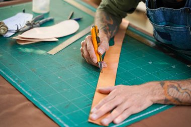 Kesici bıçak kullanan usta zanaatkârın yakın çekim ve kırpma eli atölyede kemer yapmak için deri kesti..