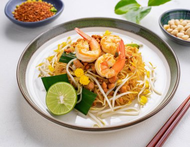 Dünyaca ünlü taze kızartılmış Tayland karidesli erişte tarifi. Beyaz seramik tabak ve kaşıkla süslenmiş sebzeli, millet. Restoran menüsü için yatay fotoğrafçılık