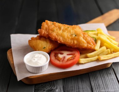 Yakın plan İngiltere ulusal gıda balığı ve patates kızartması ve krema ile ahşap tahta ve siyah arka plan servis edilir..