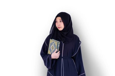 Güzel bir Müslüman öğrenci abaya niqab geleneksel giysiler giyiyor ve beyaz duvar arkasında Kur 'an' ı tutuyor. Arapça metinler İngilizce 'de şanlı Kuran' dır..