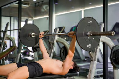 Mükemmel vücutlu Asyalı adam spor salonunda omuz ve göğüs kasları oluşturmak için halter ağırlık antrenmanı yapıyor..