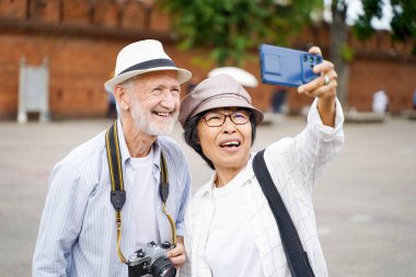 Yakın plan Amerikalı kıdemli turist ve Asyalı arkadaşı antik şehir kapısının arka planında bulanık bir fotoğraf çekiyorlar. Kıdemli turist konsepti