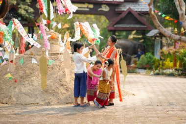 Taylandlı bir grup genç ve güzel Taylandlı bir kadın. Geleneksel Tayland elbisesi giyip Songkran festivalinde tapınakta kum yığınının üzerinde insan mağarası trencilik oynuyorlar..