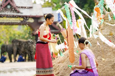 Tayland geleneksel elbiseli güzel Taylandlı kadınlar Songkran festivalinde tapınaktaki kum yığınına üçgen bayrak dikmeye yardım ediyorlar..