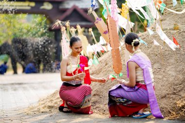 Tayland geleneksel elbiseli güzel Taylandlı kadınlar Songkran festivalinde tapınaktaki kum yığınına üçgen bayrak dikmeye yardım ediyorlar..
