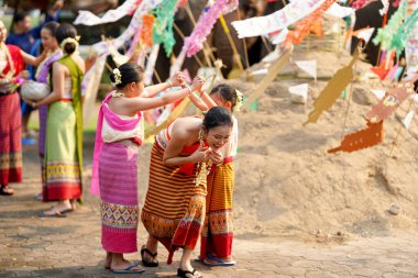 Taylandlı bir grup genç ve güzel Taylandlı bir kadın. Geleneksel Tayland elbisesi giyip Songkran festivalinde tapınakta kum yığınının üzerinde insan mağarası trencilik oynuyorlar..
