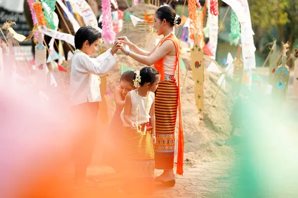 Taylandlı bir grup genç ve güzel Taylandlı bir kadın. Geleneksel Tayland elbisesi giyip Songkran festivalinde tapınakta kum yığınının üzerinde insan mağarası trencilik oynuyorlar..