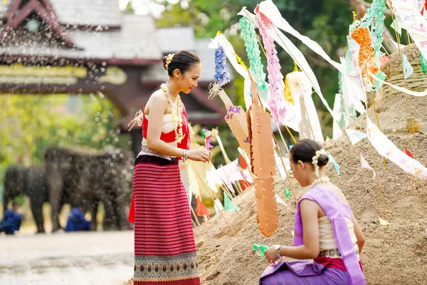 Tayland geleneksel elbiseli güzel Taylandlı kadınlar Songkran festivalinde tapınaktaki kum yığınına üçgen bayrak dikmeye yardım ediyorlar..
