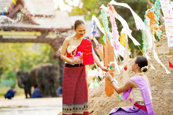 Tayland geleneksel elbiseli güzel Taylandlı kadınlar Songkran festivalinde tapınaktaki kum yığınına üçgen bayrak dikmeye yardım ediyorlar..