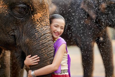 Tayland geleneksel elbisesi içinde neşeli bir Tayland kızı Tayland Songkran su festivalinde Asya filinin hortumuna sarılıyor..