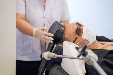 Huzurevlerindeki yaşlı hastaların kafalarına elektrik kas uyarıcısı (EMS) kullanarak yakın çekim ve ekin fizyoterapisti