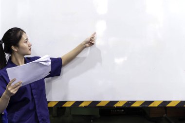 Üniformalı Asyalı kadın endüstriyel mühendis evrakları tutuyor ve boş bir beyaz tahtaya işaret ediyor, Asyalı mühendis öğretimi, bilgi kavramı,