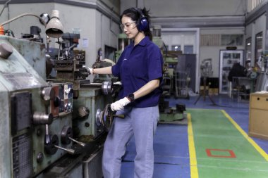 Endüstriyel atölyede eski model torna ve sondaj makinesiyle çalışan üniformalı Asyalı kadın endüstriyel mühendis..
