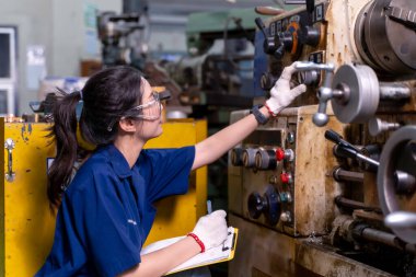 Yakın plan Asyalı endüstriyel mühendis kadın eski model torna ve sondaj makinesini endüstriyel atölyede pano ile kontrol ediyor..