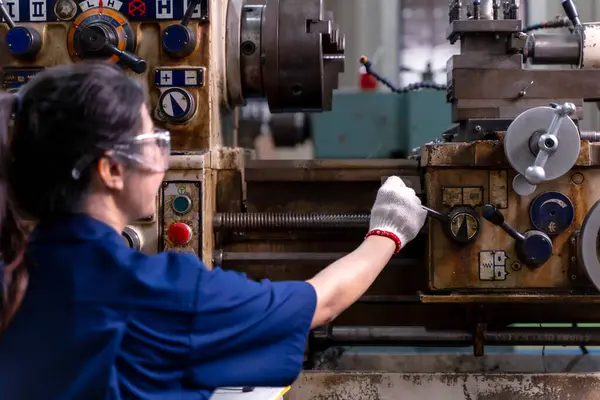 Endüstriyel atölyede eski model torna ve sondaj makinesiyle çalışan Asyalı kadın endüstriyel mühendisin yakından ve arkadan görünüşü.