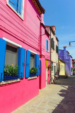 Flower pots decorate on the walls and blue windows of the pink house. Colorful architecture in Burano Island, Venice, Italy