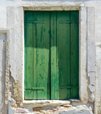 Green window on cracked concrete wall overlooking red bricks in Burano Island, Italy
