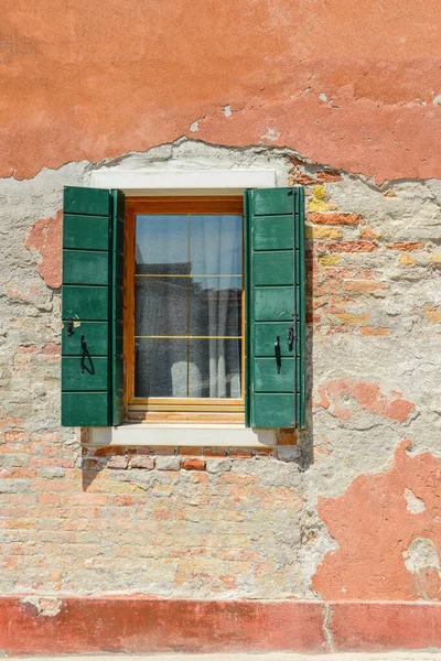 オレンジの古い家の壁の上の緑の窓イタリアのブラーノ島の具体的な可視赤レンガの亀裂 — ストック写真