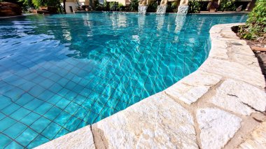 Parlak mavi yüzme havuzunun önündeki taştan sınıra yakın. Güneş ışığı yansımalı havuzların dekorasyonu ve tasarımı, tatil, rahatlama, kaçış konsepti 