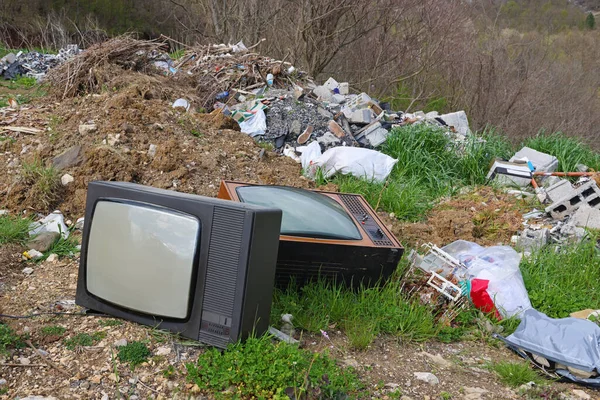 Old retro television set at a junkyard. Broken TV with garbage dump, environmental pollution