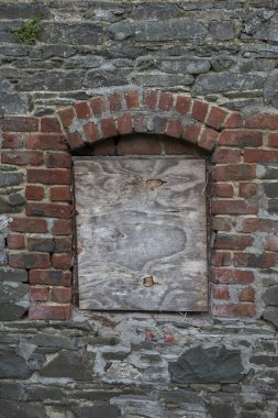 The wall of an abandoned, industrial building shows crumbling stone and brick, with boarded-up windows, evoking a sense of decay and neglect. Photo taken in Inniskeen, County Monaghan, Ireland clipart