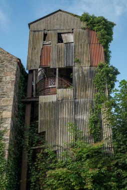 Ruined tower covered with corrugated asbestos roofing sheets and overgrown with ivy. Its weathered, crumbling walls reflect a state of neglect and industrial decay. Photo taken in Inniskeen, County Monaghan, Ireland clipart