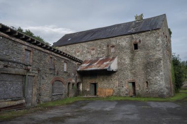 Terk edilmiş, endüstriyel bir binanın kalıntıları yıkılan taş ve tuğlaları gösteriyor. Pencereleri tahta kaplı ve sarmaşık yüzeye tırmanıyor. Çürüme ve ihmal hissi uyandırıyor. Fotoğraf Inniskeen, County Monaghan, İrlanda 'da çekildi.