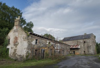 Terk edilmiş, endüstriyel bir binanın kalıntıları yıkılan taş ve tuğlaları gösteriyor. Pencereleri tahta kaplı ve sarmaşık yüzeye tırmanıyor. Çürüme ve ihmal hissi uyandırıyor. Fotoğraf Inniskeen, County Monaghan, İrlanda 'da çekildi.